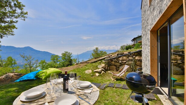 An outdoor dining setup with a table, plates, glasses, and a grill, overlooking a mountainous landscape. - COTTAGE Elena by KlabHouse-4pax w/AC & Lakeview  (Dolo)