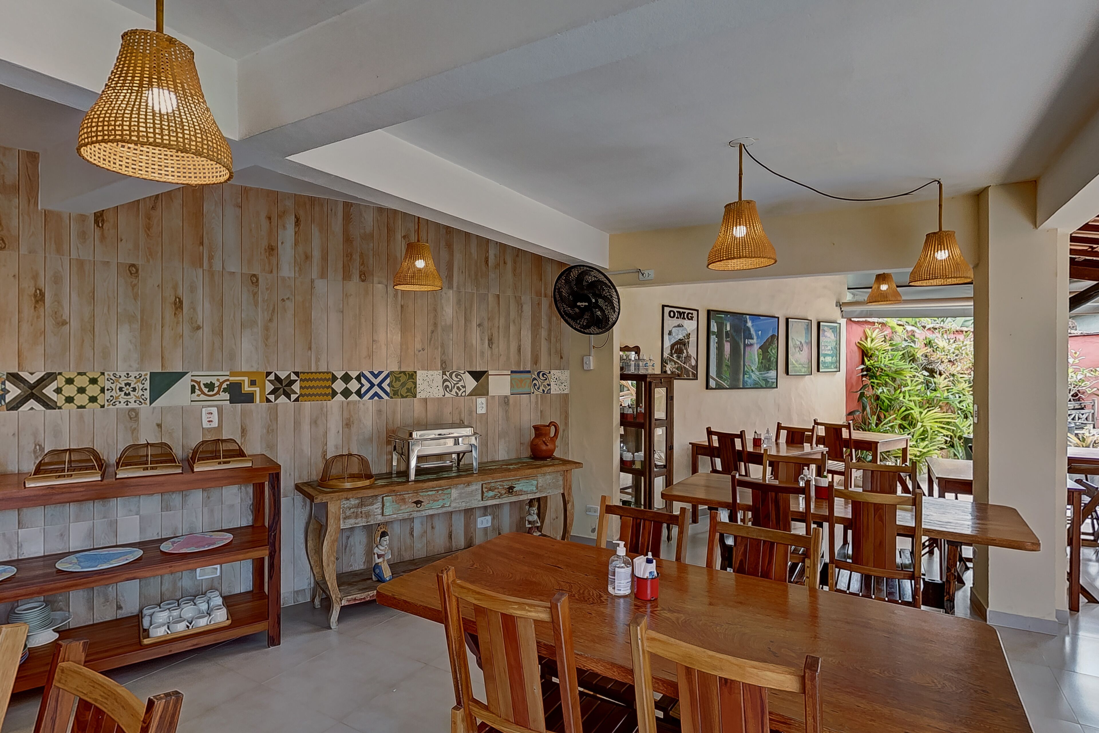 Un restaurant aux murs en bois, doté de nombreuses tables et chaises, de lampes en osier suspendues et présentant une variété de plats exposés sur des étagères.