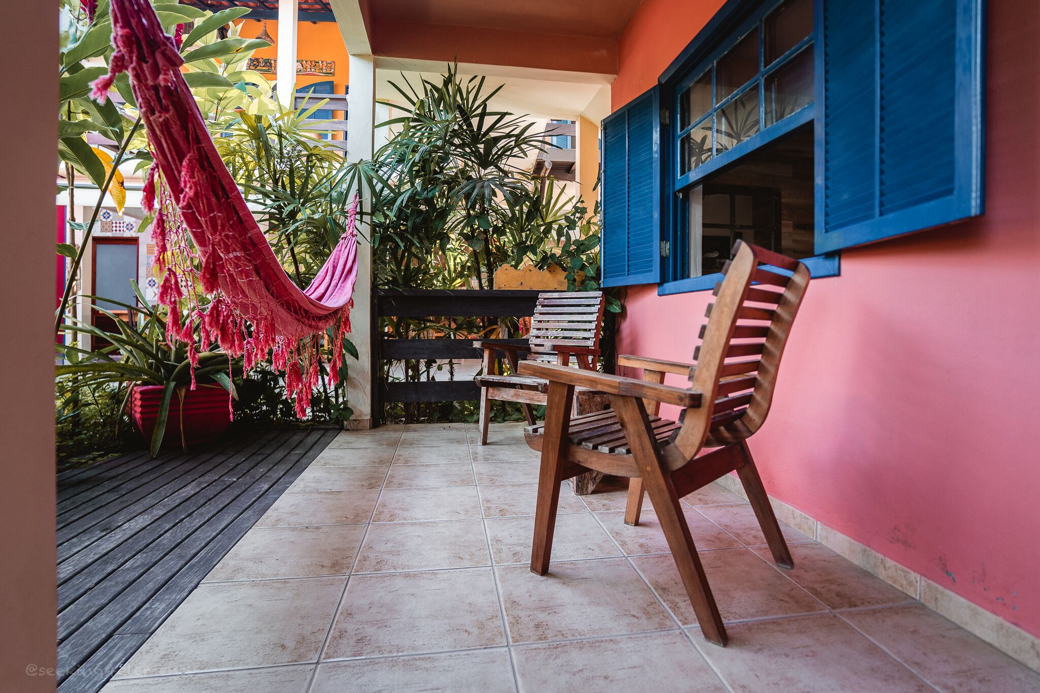 Un patio con una hamaca, sillas de madera y plantas en macetas.