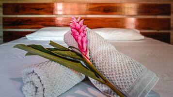 Una cama con una toalla enrollada y una flor rosa encima, frente a una pared de madera con dos cuadros enmarcados.