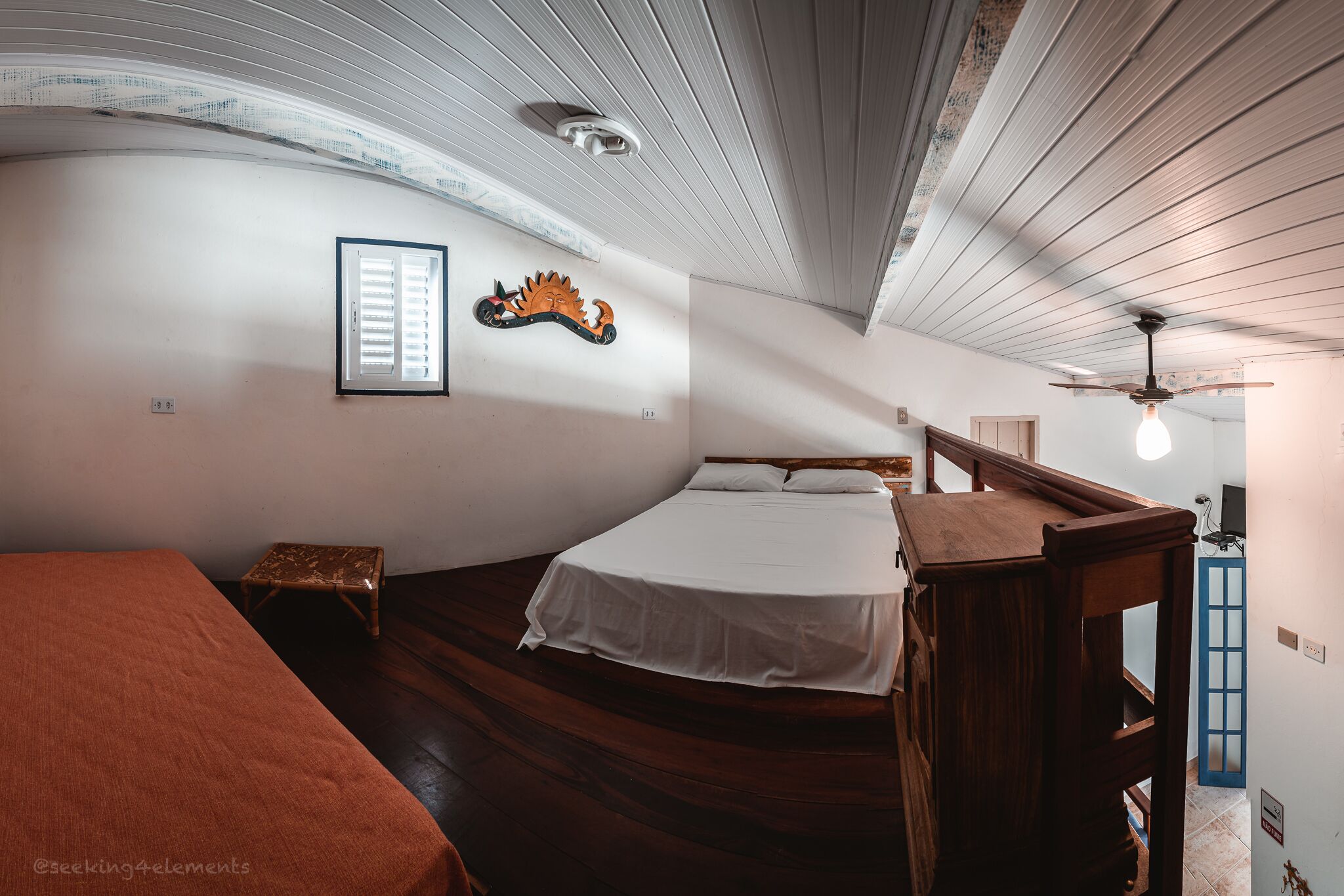A room with a bed, a small stool, a wooden bench, and a ceiling fan.
