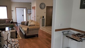 A living room with a sofa, a coffee table, and a side table with a plant. There is a door in the background and a clock on the wall. - A Wine Country  Home (Lafayette)