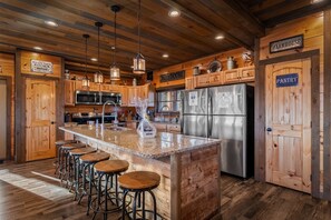 A rustic kitchen with wooden cabinets, a granite island with bar stools, stainless steel appliances, and signs indicating 'Red Oak Ranch Kitchen' and 'Farmhouse Pantry'.