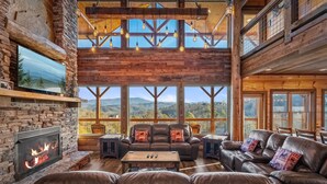 Un salon spacieux doté d’une cheminée, de canapés en cuir et de grandes fenêtres offrant une vue sur les montagnes.