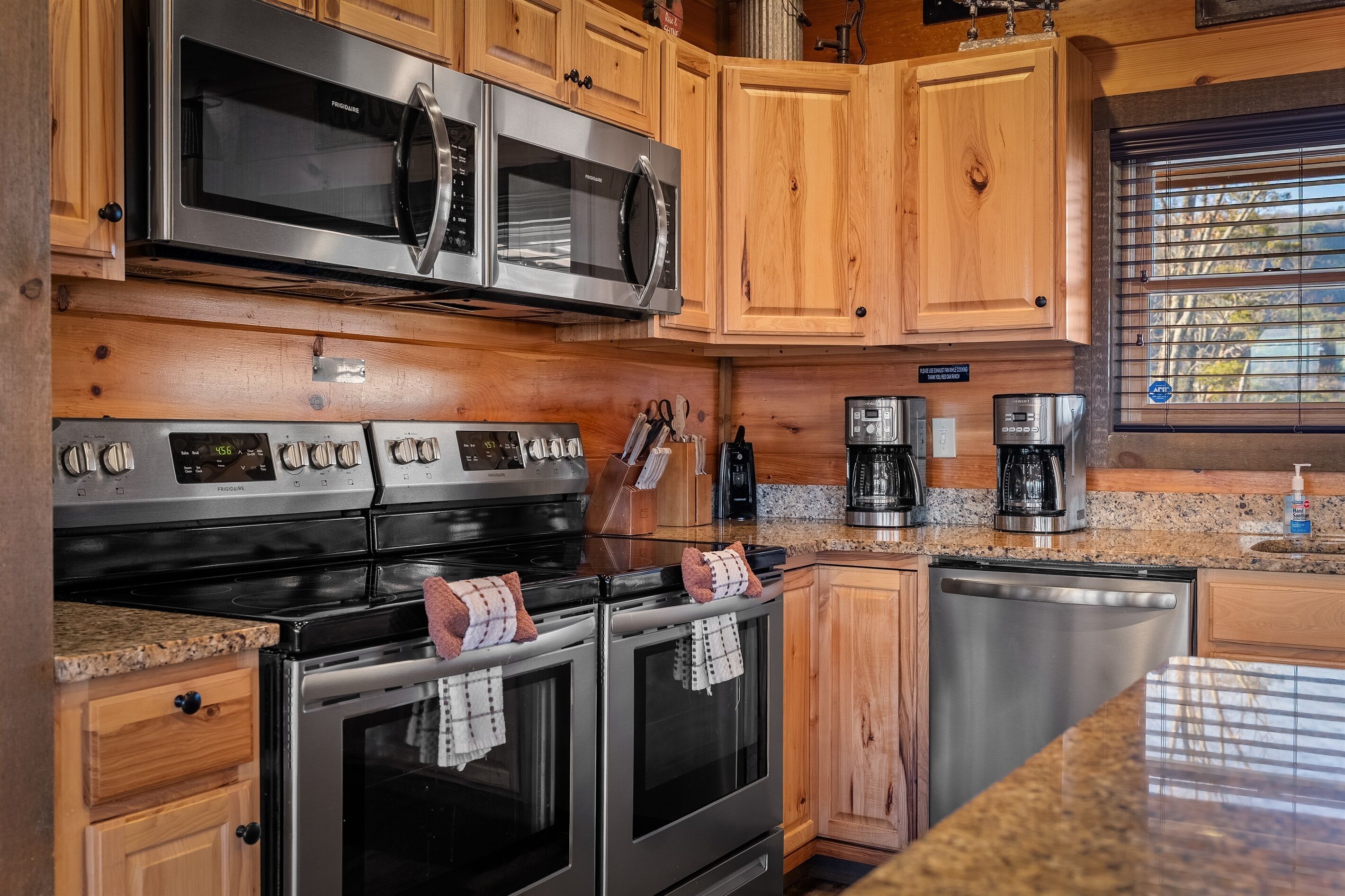 A kitchen with stainless steel appliances, wooden cabinets, granite countertops, and a window with blinds.
