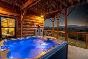 Ein Whirlpool mit Blick auf einen sternenübersäten Nachthimmel, rustikales Holzhäuschen und ein Balkon mit Geländer.