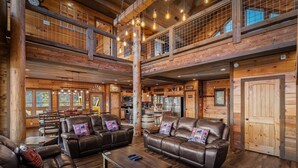 Un intérieur spacieux de chalet en bois, avec des canapés en cuir, un coin repas et une cuisine.