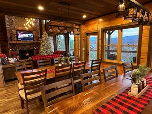 Ein gemütlicher Essbereich mit Holztisch und -stühlen, einem Kamin und einem großen Fenster mit Blick auf die Berge.