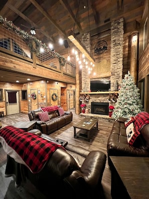 A spacious living room with a fireplace, leather sofas, and a Christmas tree.