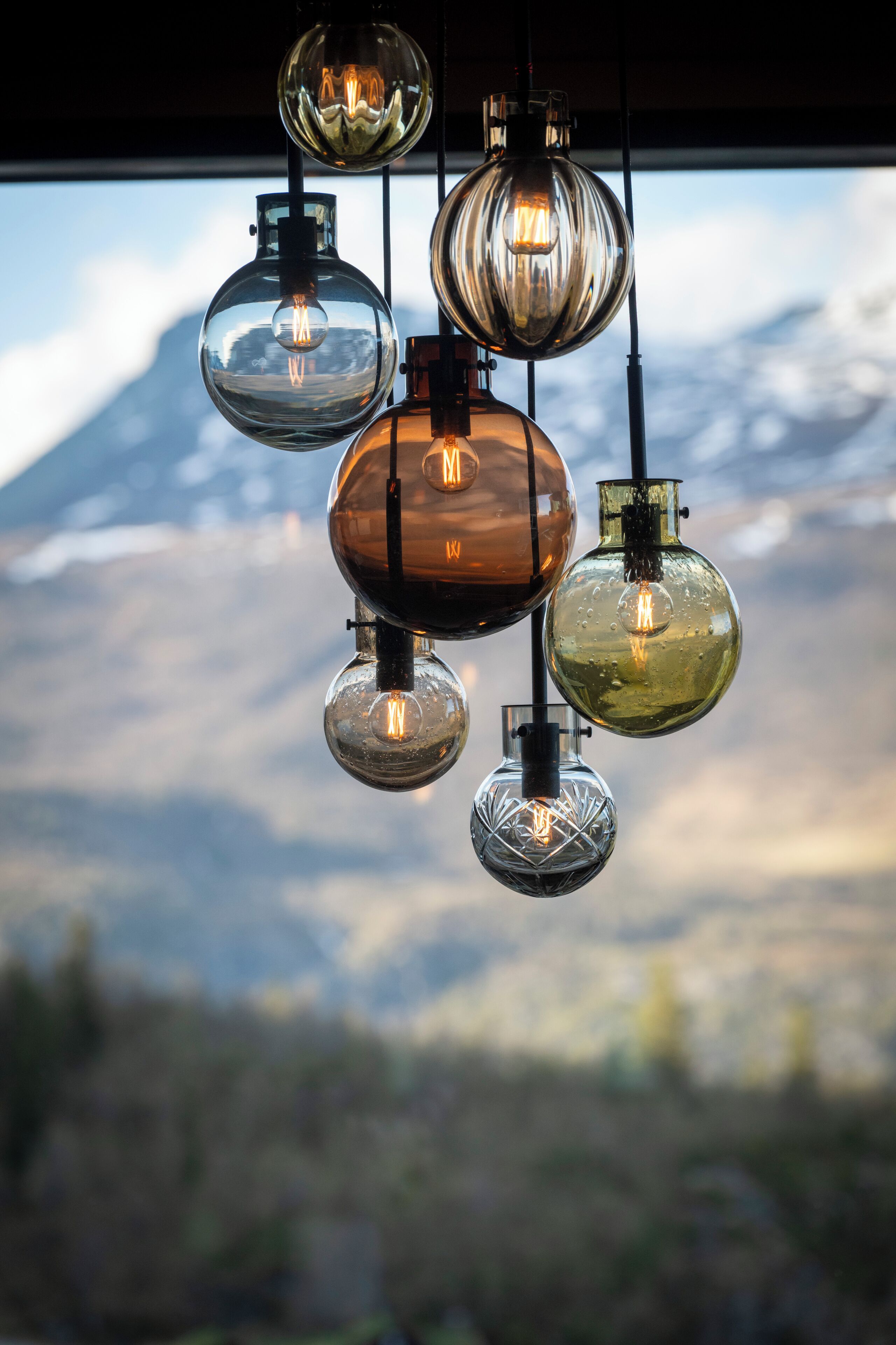 A series of spherical pendant lights with visible filament bulbs against a mountainous backdrop.