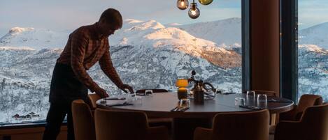 A dining area with a large window overlooking a snowy mountain landscape.