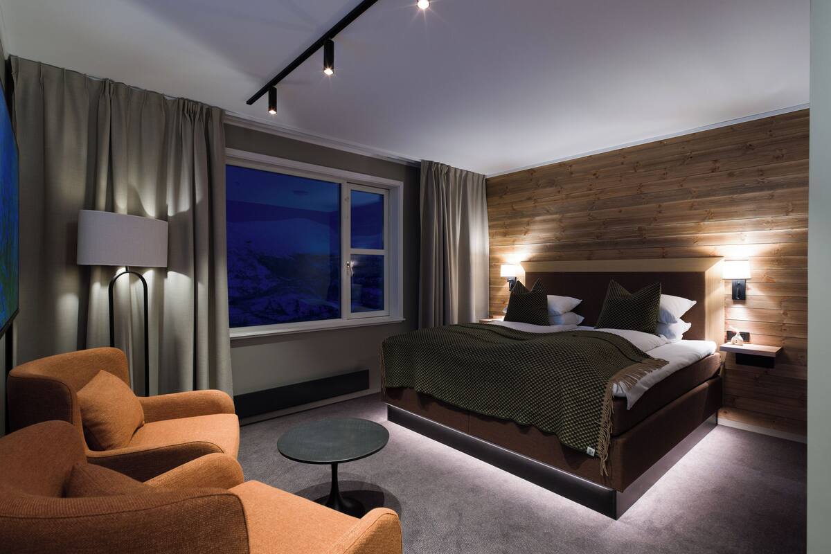 Una habitación de hotel moderna con una cama grande, una mesita redonda pequeña, un sofá y una ventana con cortinas.