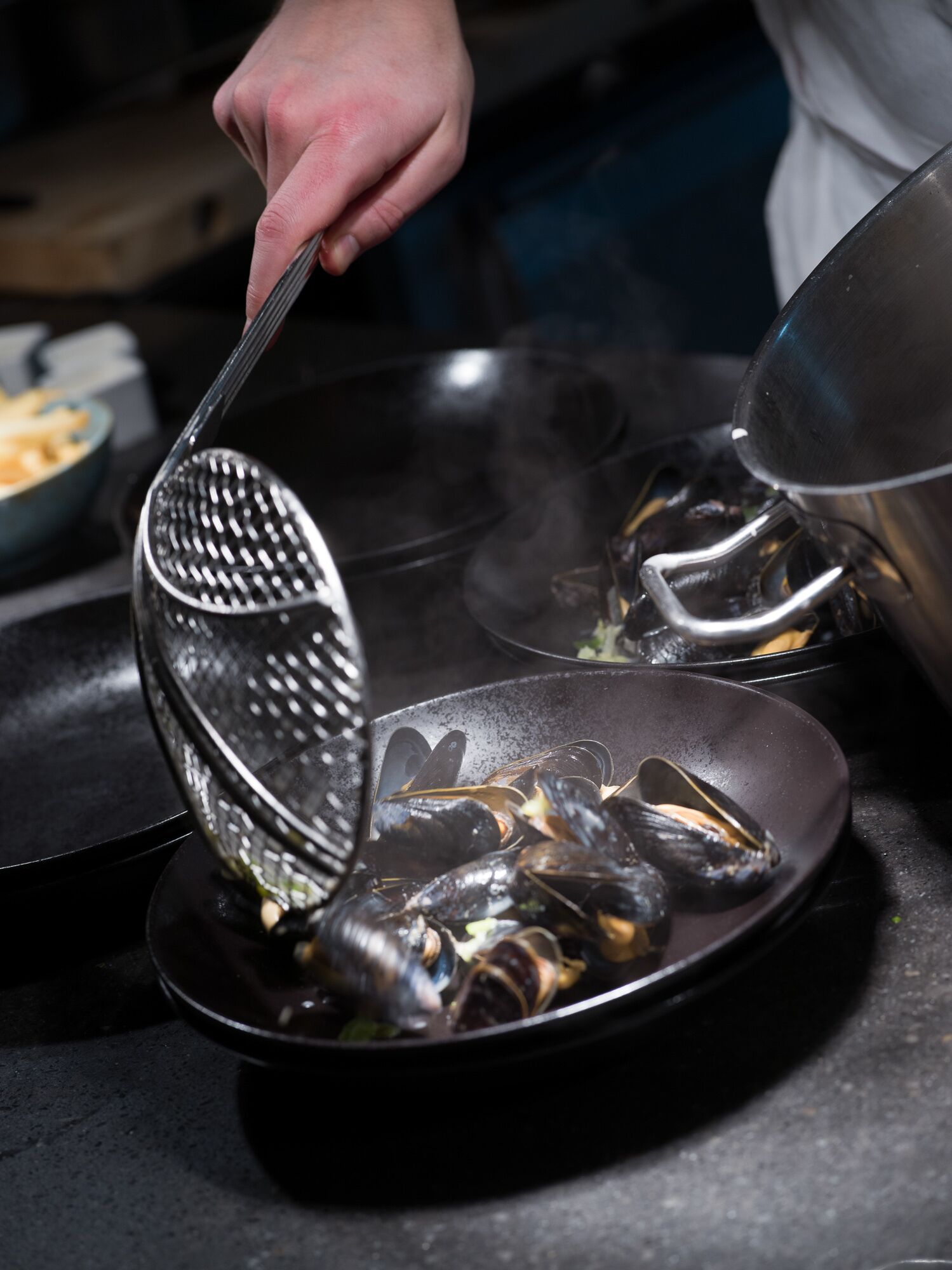 A person cooking mussels in a pan on a stove.