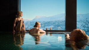 A person sitting in a pool with a view of snow-capped mountains through a large window.
