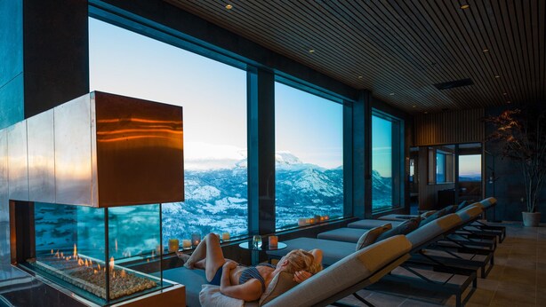 A spa area with a fireplace, reclining chairs, and a view of snow-capped mountains.