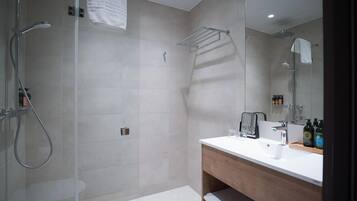 Un baño moderno con ducha envuelta en vidrio, tocador de madera con espejo y perchero.