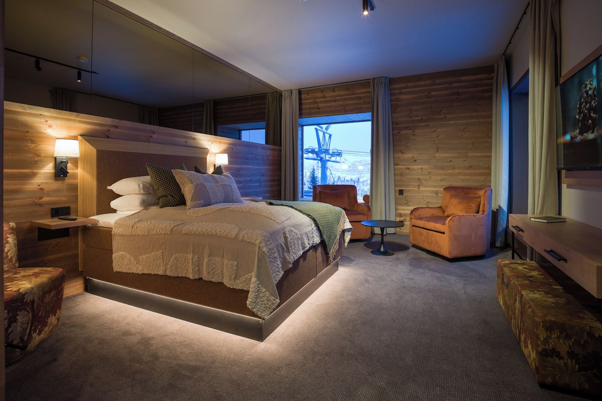 Un dormitorio moderno con una cama grande, una mesita de noche, una silla, una pequeña mesa y un televisor.
