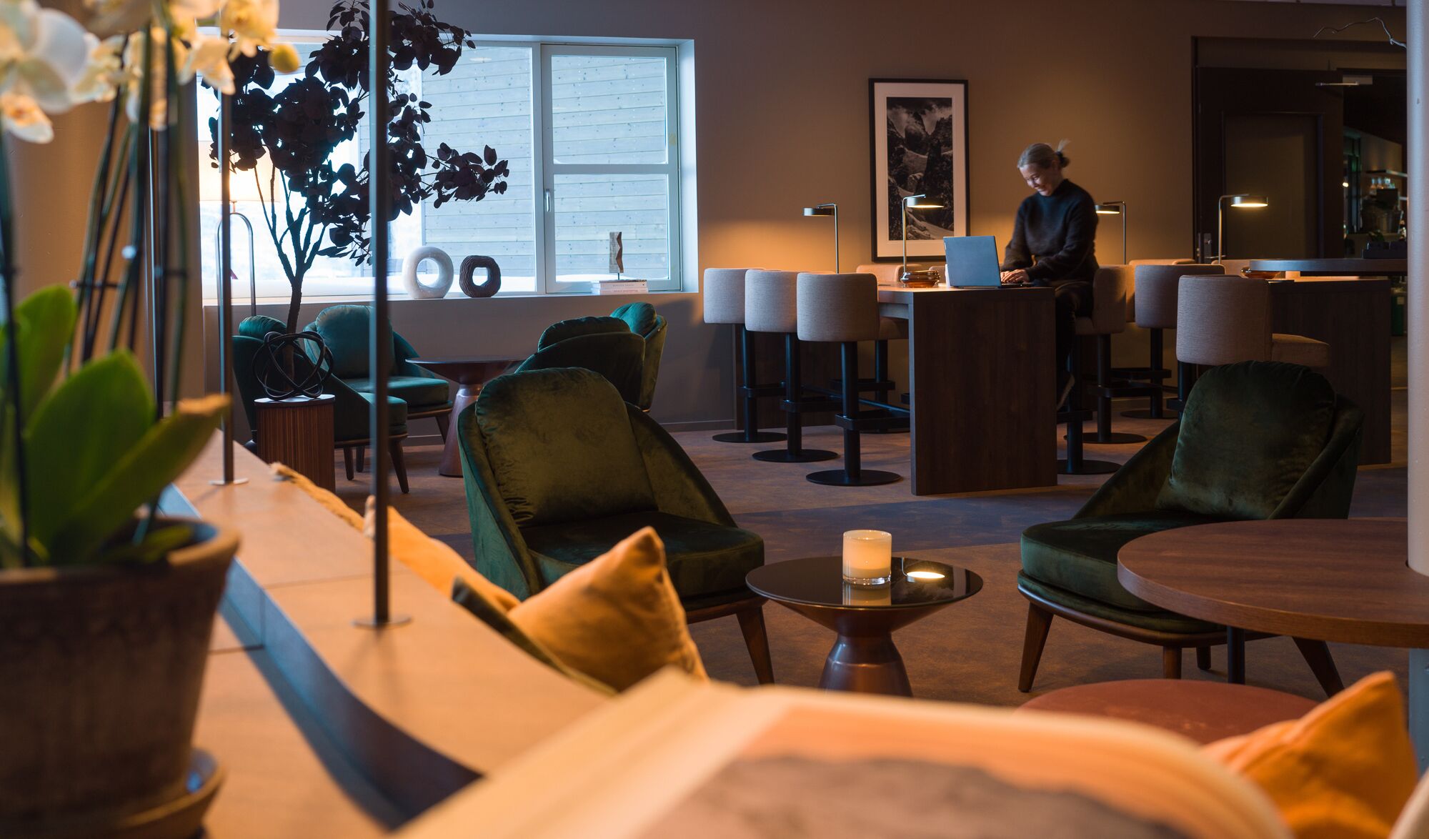 Eine moderne Lounge mit grün gepolsterten Sesseln, einer Bar und einem großen Fenster für natürliches Licht.