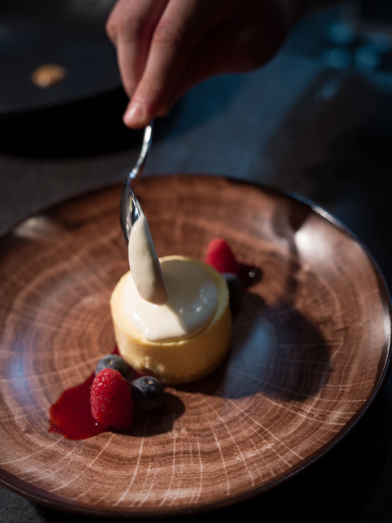A dessert on a plate with a spoon, surrounded by berries.
