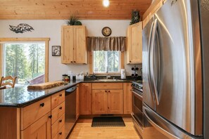 A kitchen with wooden cabinets, a stainless steel refrigerator, a built-in oven, and a window with blinds.