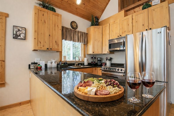 A modern kitchen with wooden cabinets, stainless steel appliances, and a central island with a charcuterie board and wine glasses.