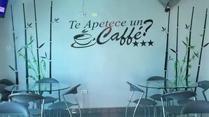 Interior de una cafetería con un adorno en la pared que dice “¿Te Apetece un Caffe?” rodeado de mesas y sillas de vidrio.