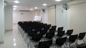 Un salón de conferencias con filas de sillas negras, una pizarra y una pantalla de proyector.