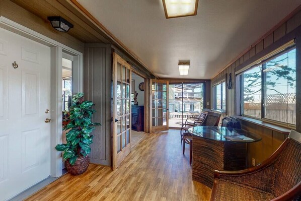 A spacious room with a wooden floor, a glass table, wicker chairs, and a large window offering a view of the outdoors.