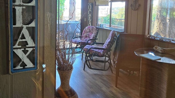 Una habitación acogedora con suelo de madera, un ventanal grande, un cartel que dice 'RELAX' y un jarrón rústico.