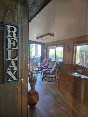 A cozy room with wooden flooring, a large window, a 'RELAX' sign, and a rustic vase.