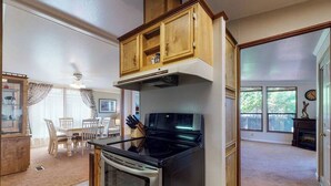 Una cocina con estufa, horno y armarios de madera. Hay un comedor con mesa y sillas.