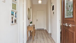 Un couloir avec un plancher en bois, une porte blanche au fond, une petite table avec une plante et un miroir fixé au mur.