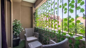 A balcony with wicker furniture, a potted plant, and a view of buildings through a metal fence with green foliage. - Cosy Hyper center Bd Hassan 2 (Marrakech)