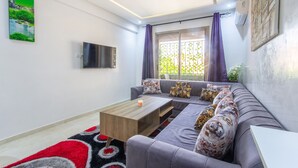 A modern living room with a grey sofa, a wooden coffee table, and a flat-screen TV mounted on the wall. - Cosy Hyper center Bd Hassan 2 (Marrakech)