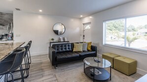 A modern living room with a black leather sofa, a round coffee table, and a dining area with bar stools. - Beach Oasis with Private Pool (Fort Lauderdale)