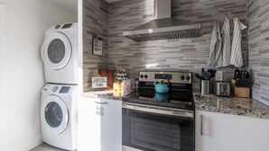 A compact kitchen with a washing machine, a stove, and a coffee sign. - Beach Oasis with Private Pool (Fort Lauderdale)