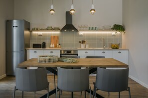 Eine moderne Küche mit einem Holztisch, grauen Stühlen, einem Edelstahlkühlschrank und einer strukturierten Spritzschutzwand.