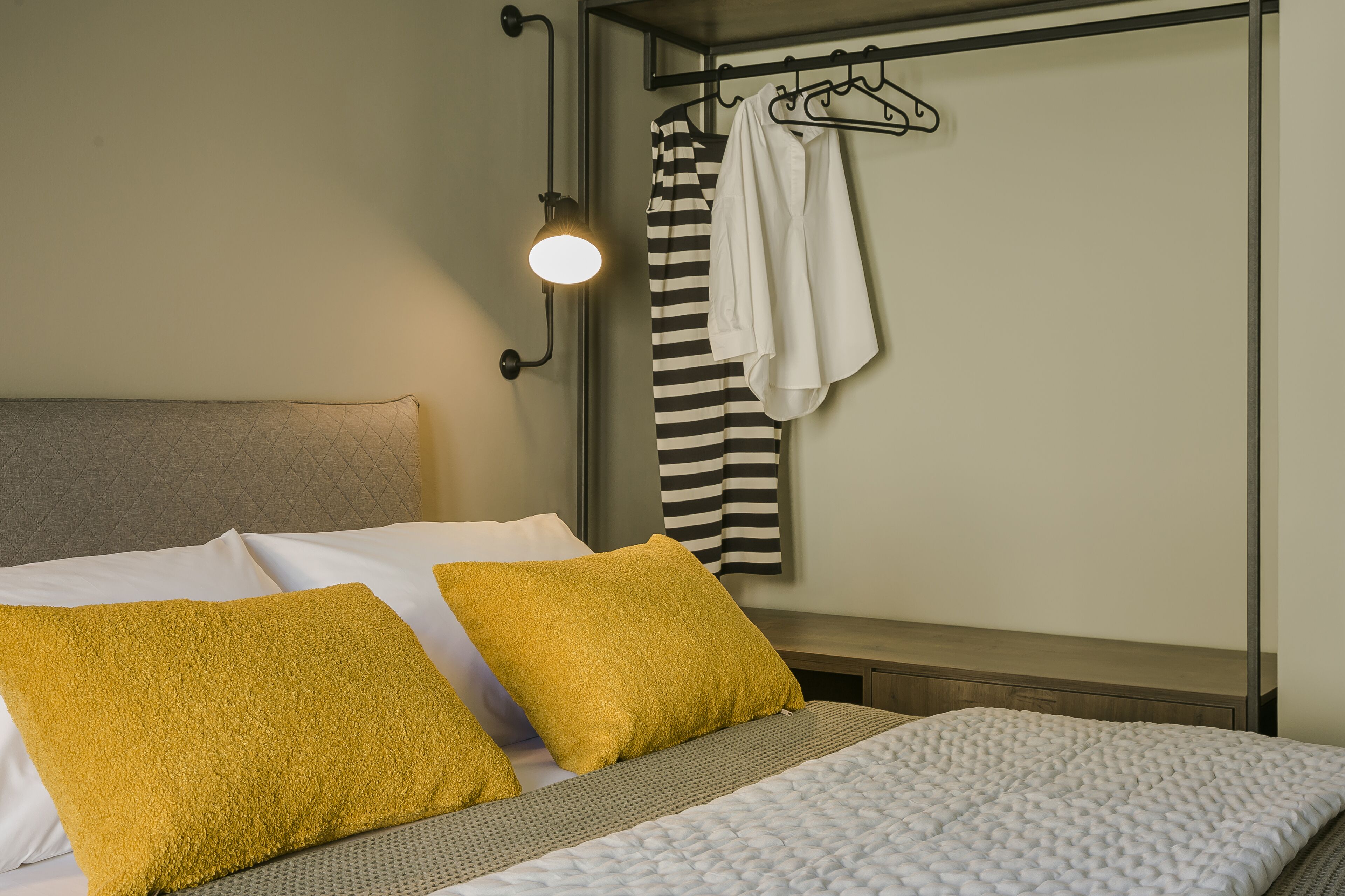 Un lit bien fait avec deux oreillers, un porte-serviettes mural avec une serviette, et un luminaire fixé au mur.