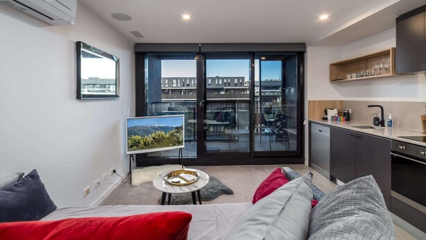 Eine moderne Wohnung mit Balkon, einer Küche und einem Wohnbereich mit Sofa und Fernseher.