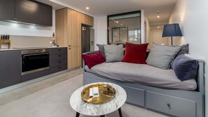 Ein modernes Wohnzimmer mit einer Couch, einem Couchtisch und einer Küchenzeile mit Schränken und Geräten.