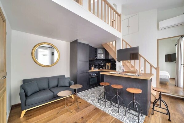 A modern apartment with a living area, kitchen, and a staircase.