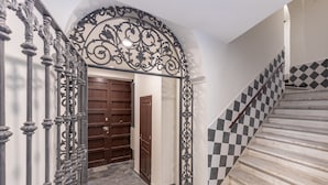 A hallway with a decorative metal gate, a wooden door, and a staircase with checkered tiles. - Líbere Málaga La Merced (Málaga)