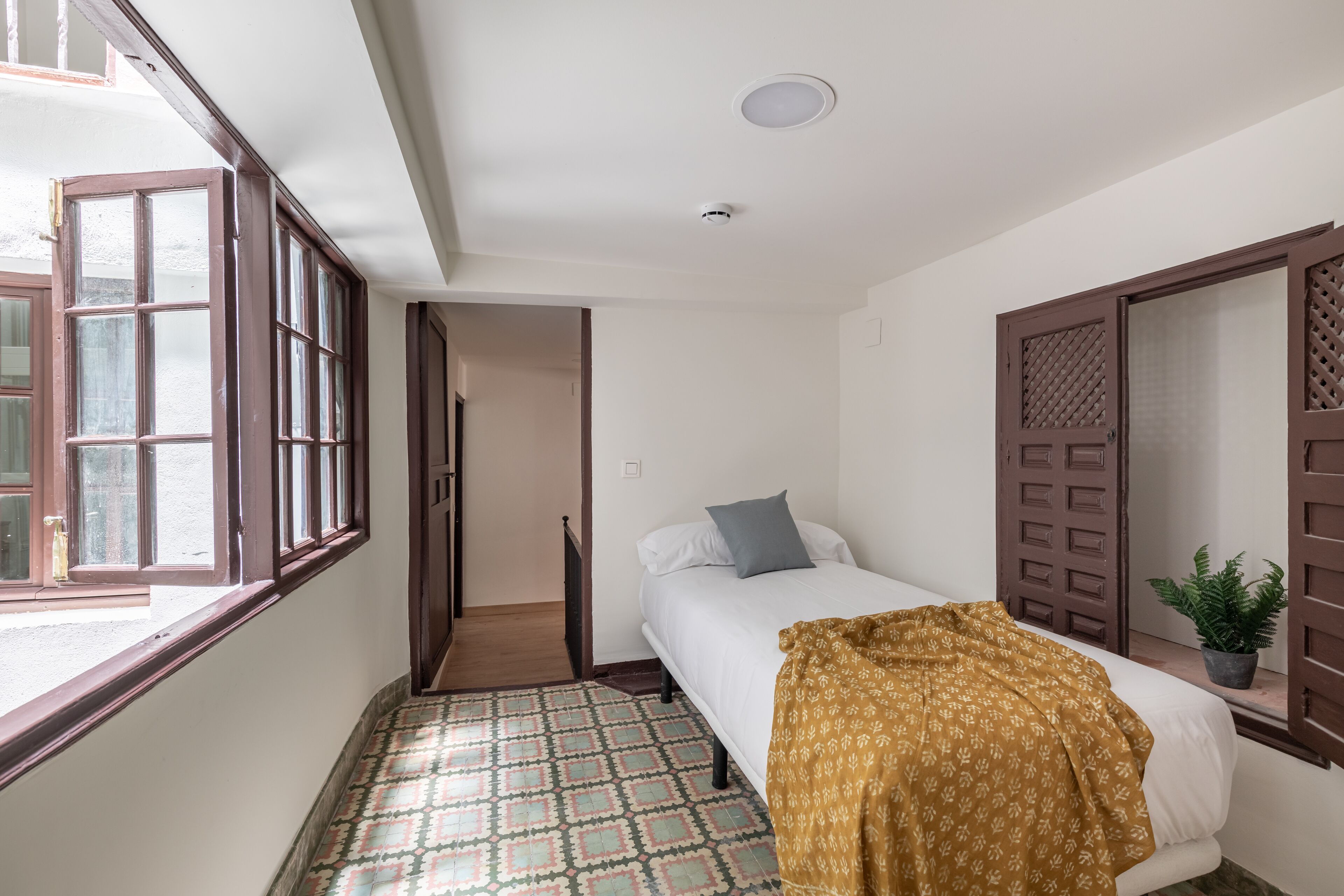Quarto com cama, janela, porta e planta em vaso.