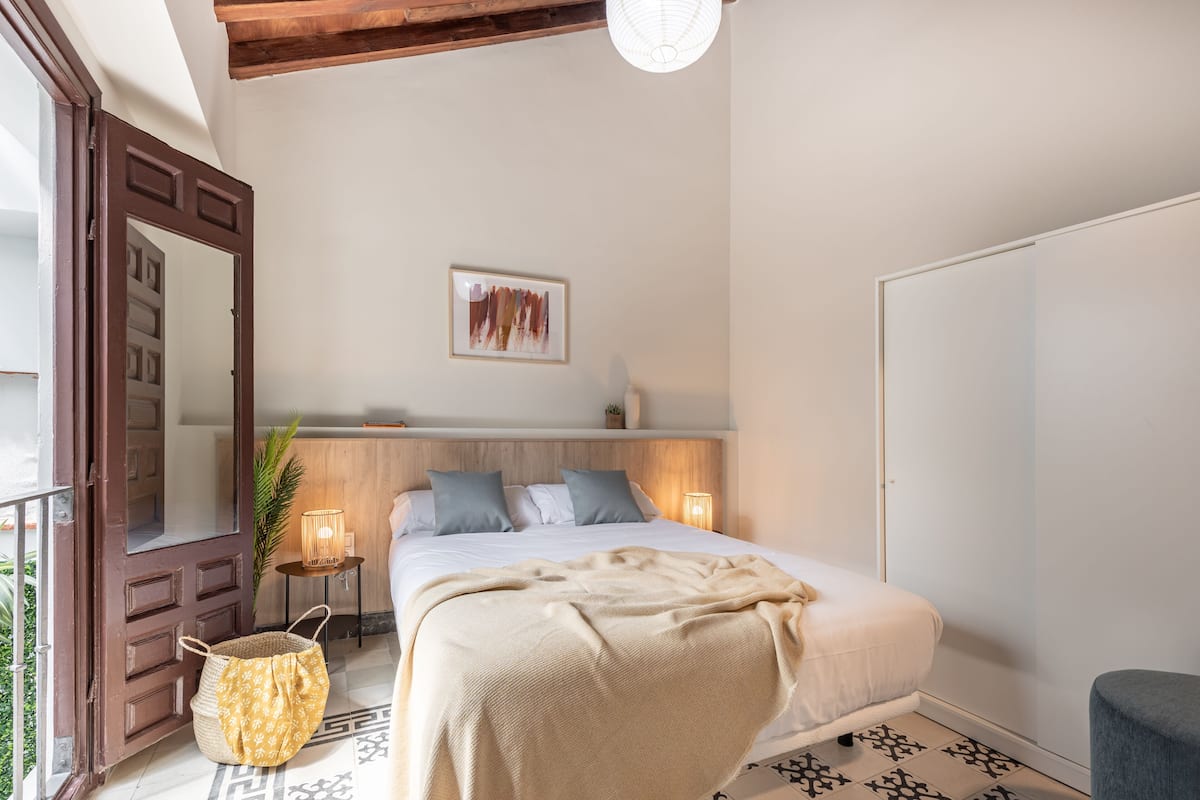 Quarto com cama, abajures, espelho, quadro na parede e cesta no chão.