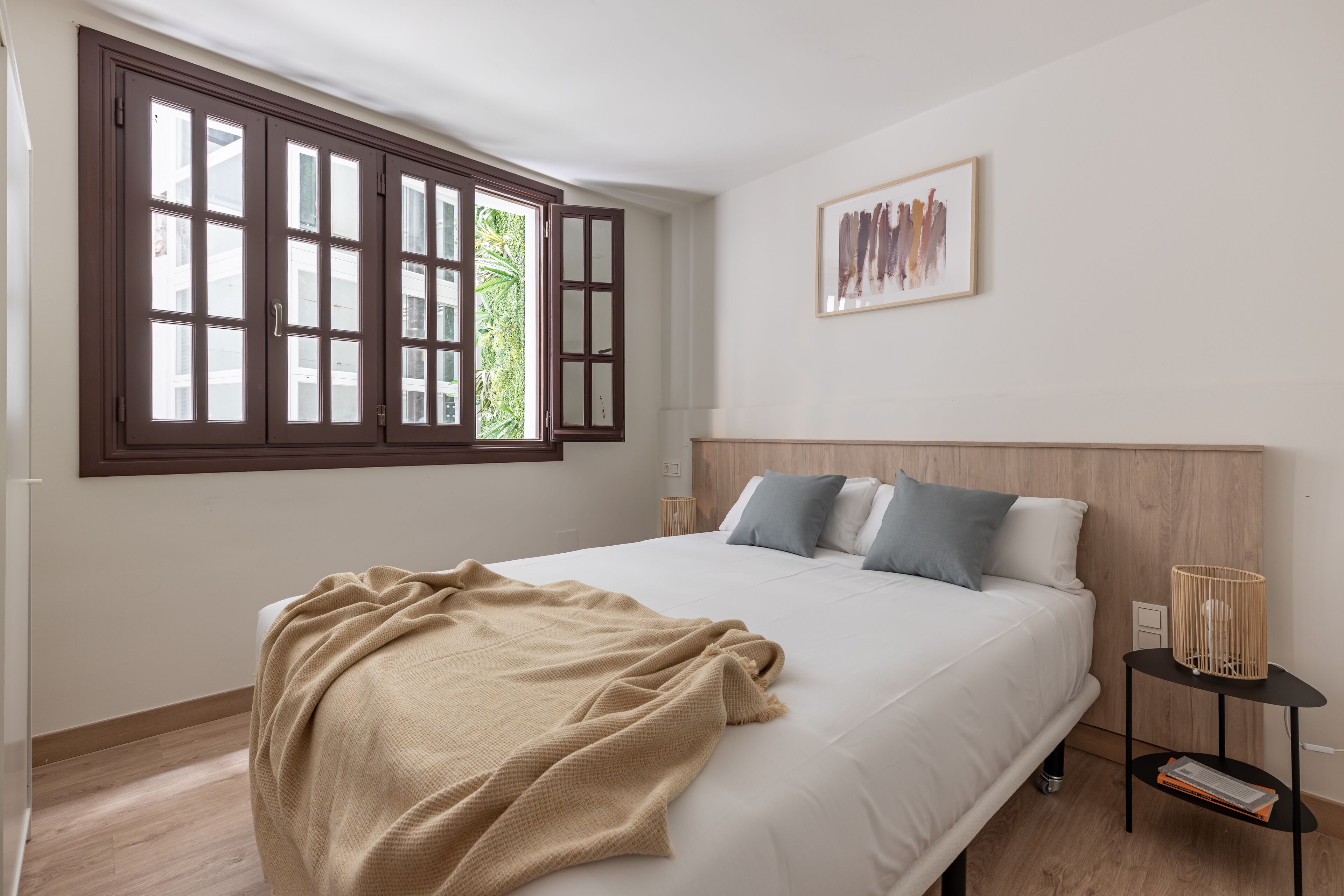 Un dormitorio con una cama grande, una ventana con múltiples vidrios, una mesita de noche con lámpara y un cuadro en la pared.