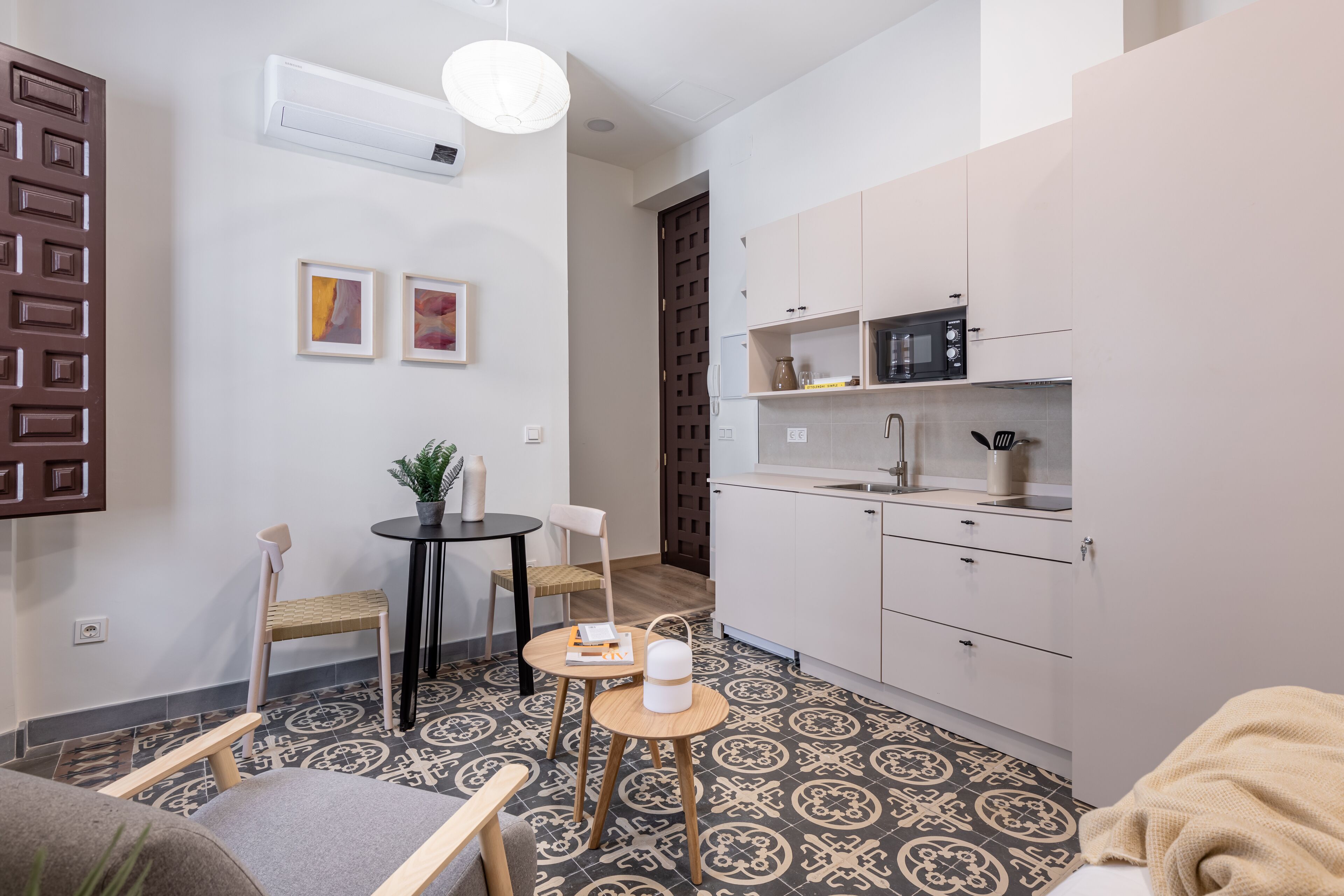 A compact living space with a kitchenette, a dining area with two chairs, and a small table with a plant.