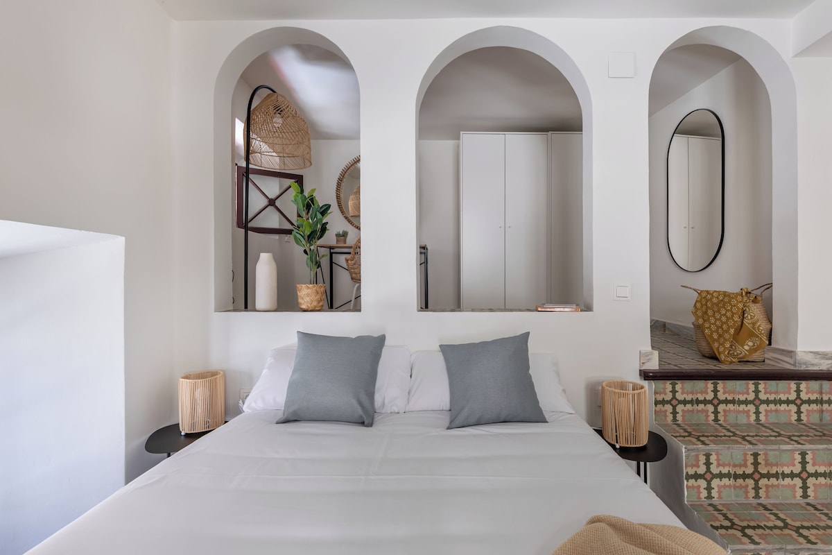 A modern bedroom with a large bed, two bedside tables, a mirror, and a wardrobe.