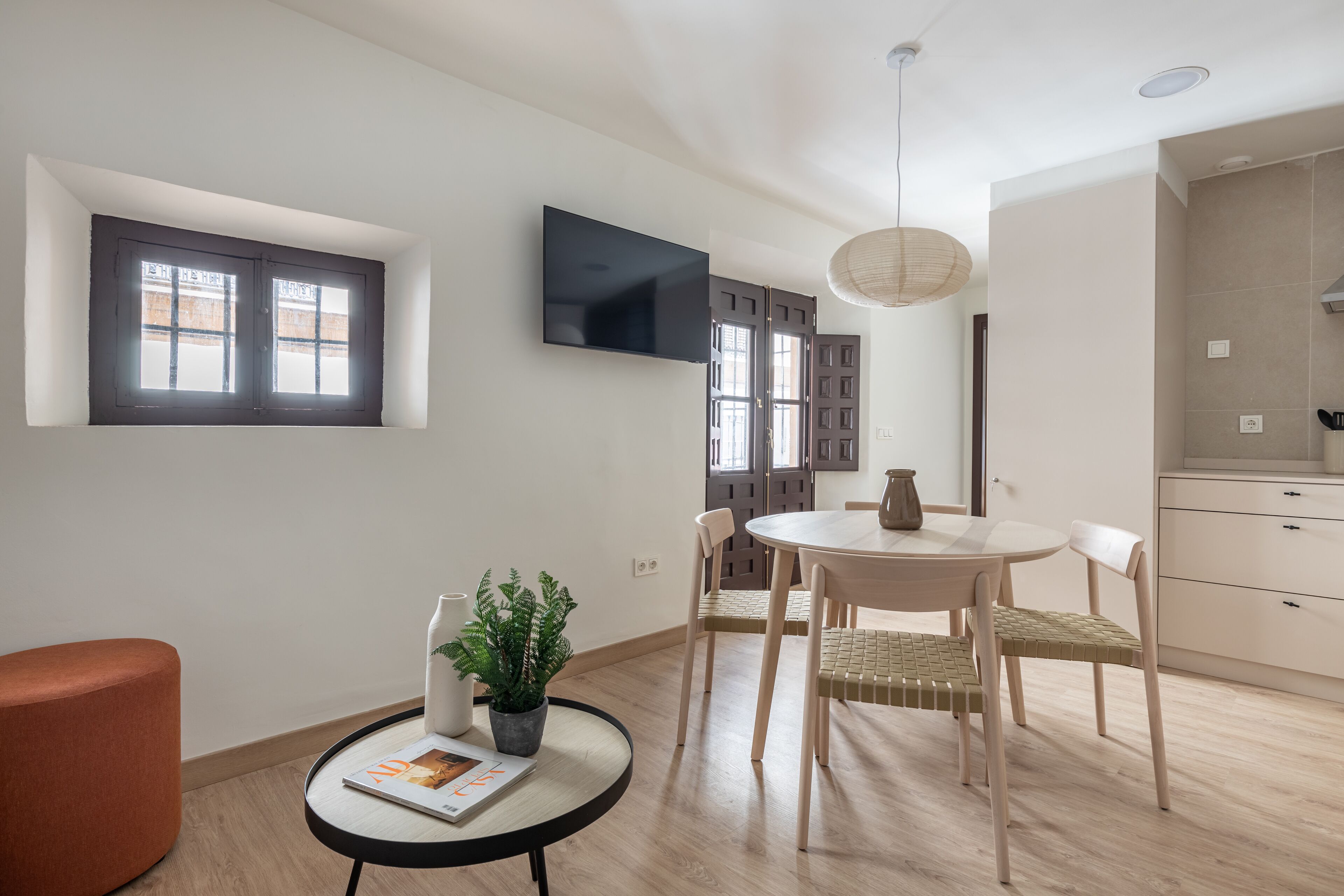Un salon moderne avec une table à manger ronde, deux chaises, un canapé, une plante en pot et un téléviseur à écran plat fixé au mur.