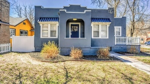 Una casa de dos pisos con fachada gris oscuro, puerta azul y un pequeño porche con barandilla blanca.