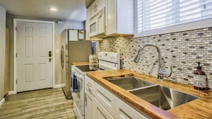 Una cocina con armarios blancos, un lavamanos de acero inoxidable y salpicadero de azulejos.